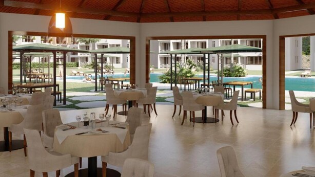 Un vaste espace dédié à la salle à manger, avec des tables et des chaises, de grands parasols, et une vue sur une piscine et les bâtiments du complexe hôtelier.