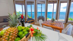 A dining area with a view of the ocean, a wooden table, and a sofa with a view. - Awesome Over The Water Overlooking West End - Aire Agua 3 Bedroom Home by RedAwning (Roatan)
