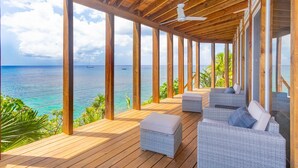 A wooden deck with wicker furniture overlooking a turquoise sea. - Awesome Over The Water Overlooking West End - Aire Agua 3 Bedroom Home by RedAwning (Roatan)