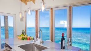 Une cuisine avec une grande fenêtre donnant sur la mer, un évier et une bouteille de vin.