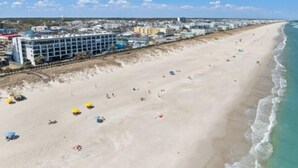 A beach with a row of buildings, including a hotel with a pool area. - Southern Comfort - Expansive Views Of The Ocean And Beach! Newly Renovated Plus Top Grade Linens! 2 Bedroom Condo by RedAwning (Carolina Beach)