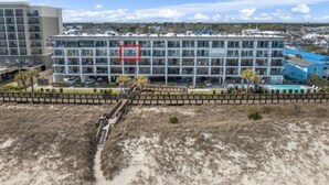 A modern multi-story hotel with a central courtyard, surrounded by a sandy landscape. - Southern Comfort - Expansive Views Of The Ocean And Beach! Newly Renovated Plus Top Grade Linens! 2 Bedroom Condo by RedAwning (Carolina Beach)