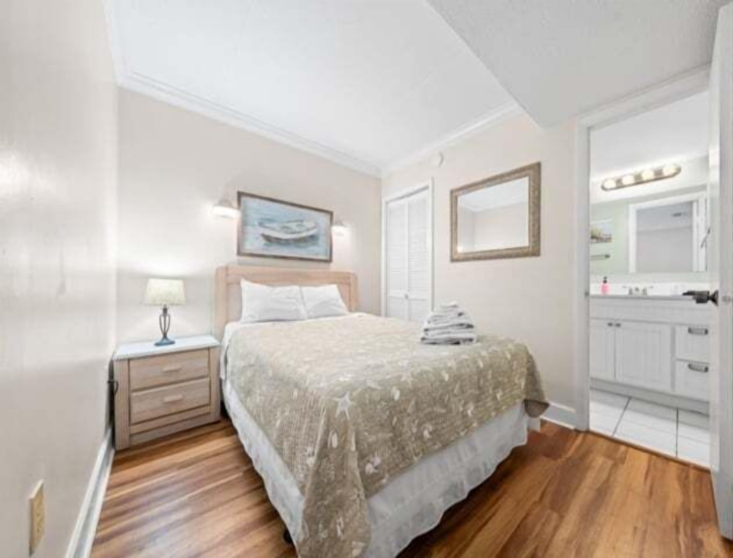 Un dormitorio con cama, mesita de noche y baño visible a través de una puerta abierta.