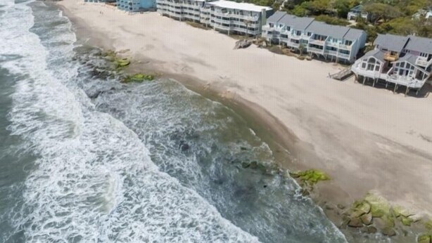 Ein Hotel direkt am Strand mit mehreren Gebäuden, einem Sandstrand und brechenden Wellen.