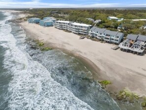 A beachfront hotel with multiple buildings, a sandy beach, and waves crashing onto the shore. - Atlantis Blue - Relaxing Beach Getaway Home Directly Across The Street From Beach Access! 5 Bedroom Home by RedAwning (Kure Beach)