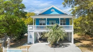 Ein zweistöckiges Haus mit blauer Fassade, einer Veranda und einem weißen Zaun.