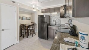 A modern kitchen with granite countertops, stainless steel appliances, and a dining area with wooden chairs. - Life's A Beach - Walk To Everything In Historic Carolina Beach! 1 Bedroom Condo by RedAwning (Carolina Beach)