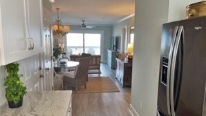 A modern kitchen with a large refrigerator, wooden flooring, and a dining area with a chandelier. - Driftwood Cottage - First Floor Oceanfront Beach Retreat! Exceptional Views, Location And Privacy 2 Bedroom Condo by RedAwning (Carolina Beach)