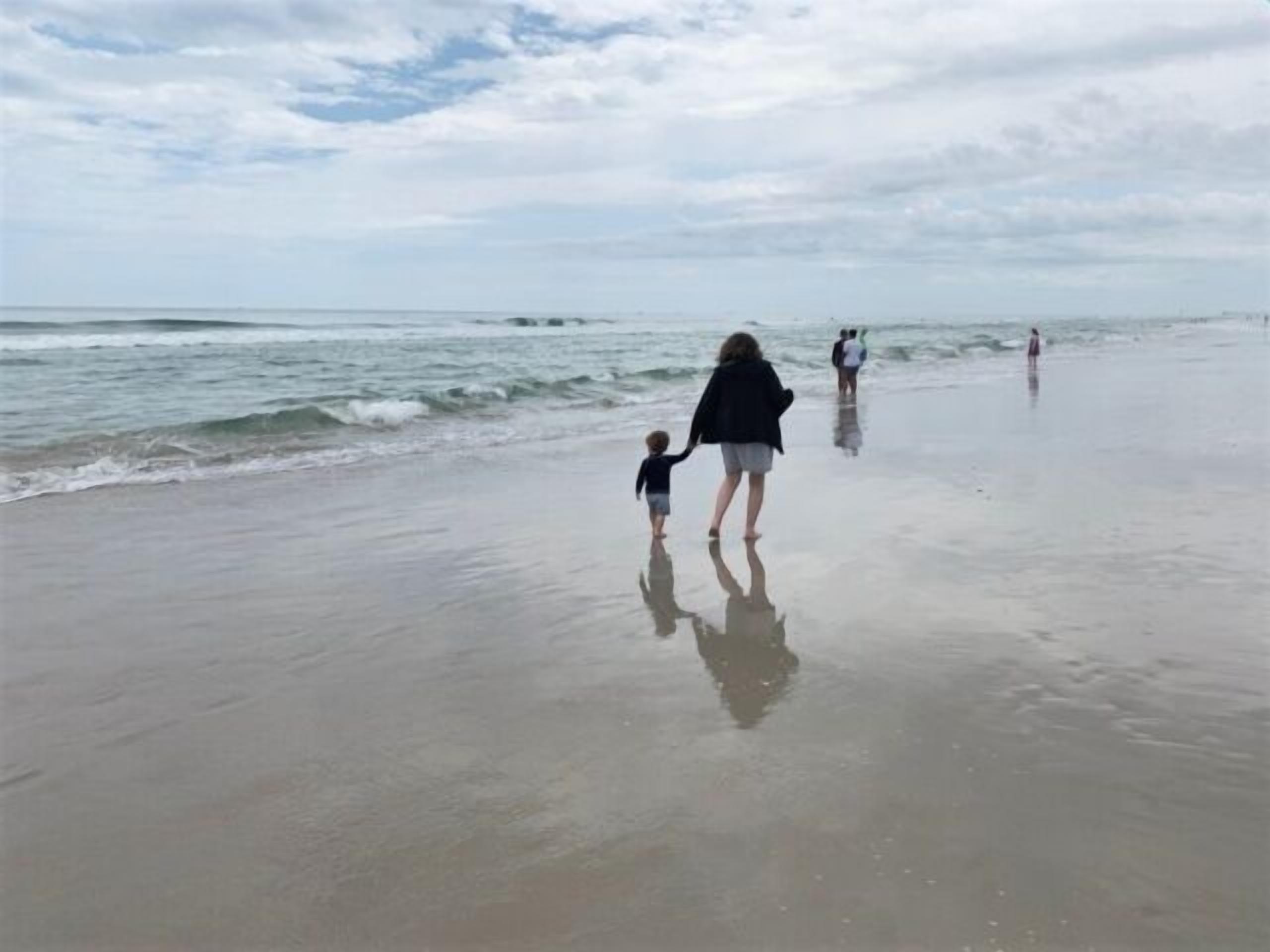 Eine Strandansicht, auf der eine Person und ein Kind am Ufer entlanggehen.