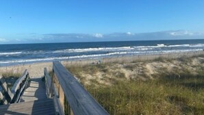 A wooden boardwalk leading to a beach with waves crashing onto the shore. - Driftwood Cottage - First Floor Oceanfront Beach Retreat! Exceptional Views, Location And Privacy 2 Bedroom Condo by RedAwning (Carolina Beach)