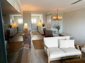 Un salon moderne avec un canapé blanc, un coin repas comprenant une table et des chaises, et un lustre.