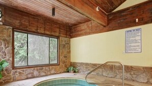 A stone-walled indoor hot tub with a wooden ceiling and a large window.