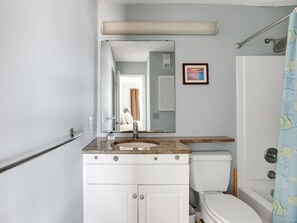 A bathroom with a white sink, mirror, and toilet. There is a shower curtain with a pattern, and a framed picture on the wall. - Beach Blanket - Spacious Condo With Private Beach Access And Resort Amenities! 3 Bedroom Condo by RedAwning (Kure Beach)