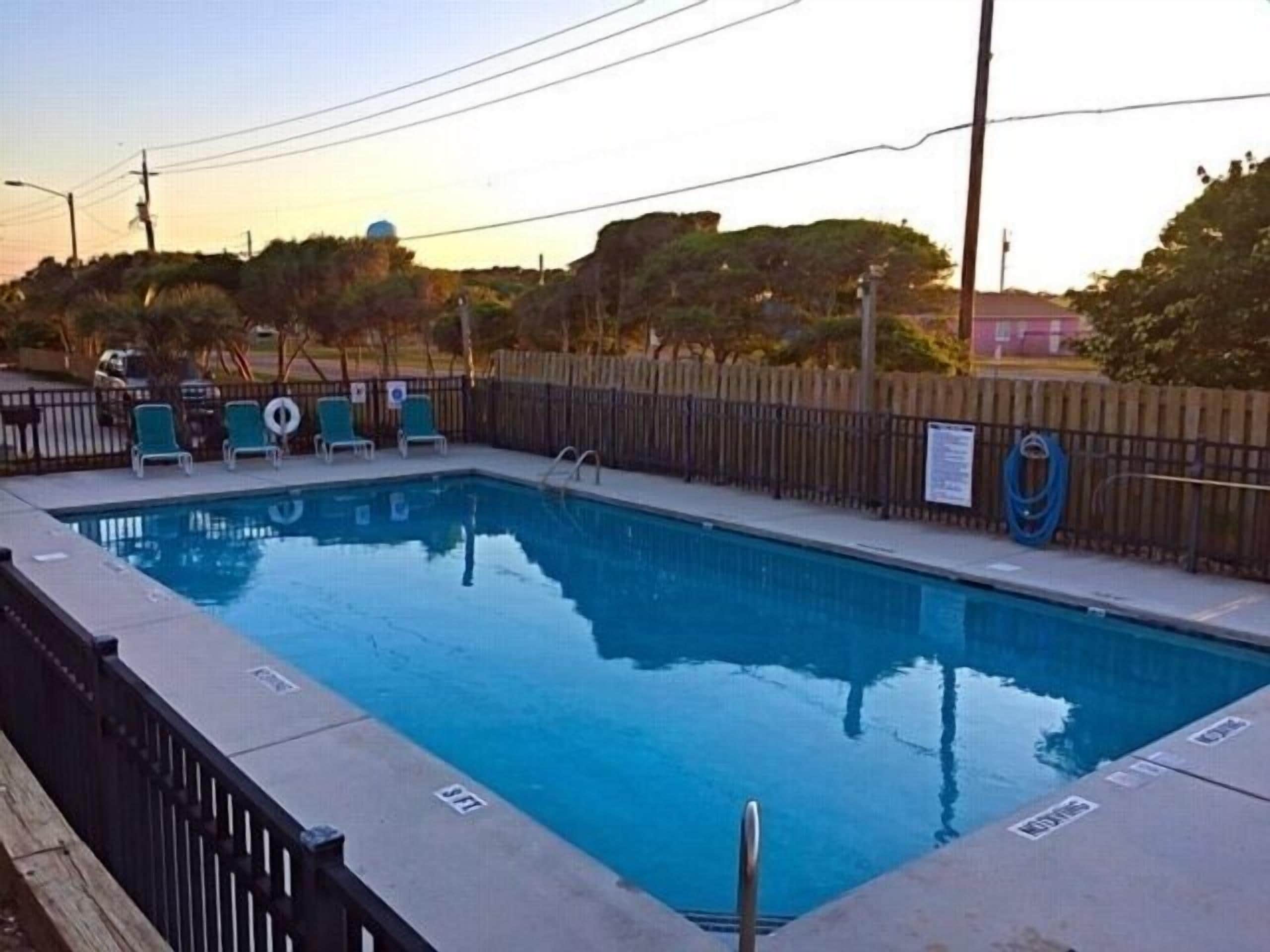 A swimming pool with a wooden fence, lounge chairs, and a lifeguard stand.