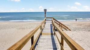 A wooden boardwalk leading to a beach with a clear sky and calm sea.