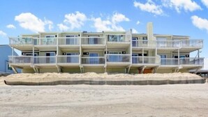 A multi-story beachfront hotel with balconies, a sandy beach in front, and a clear sky.