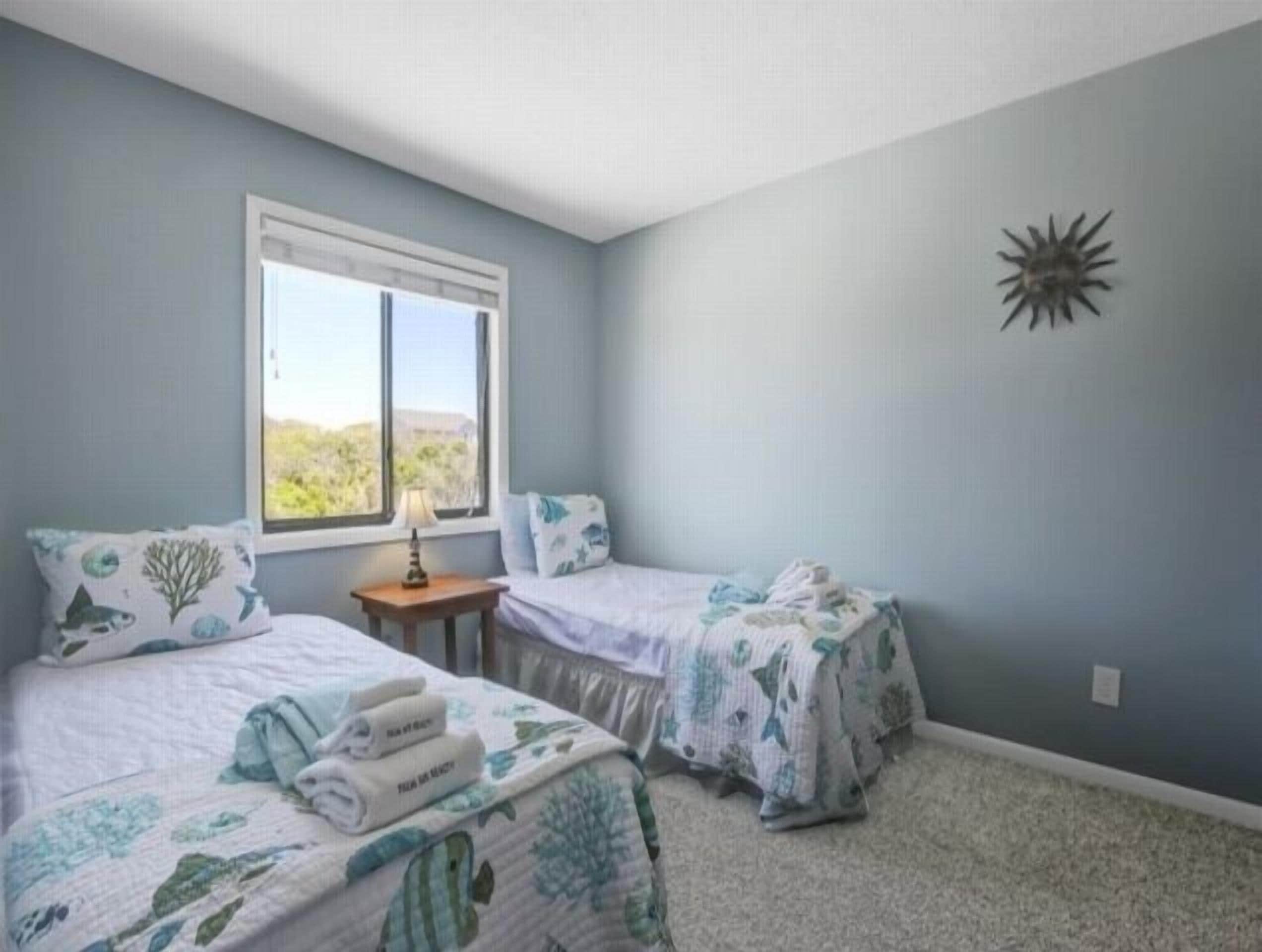 A bedroom with two beds, a window, and a decorative wall piece.