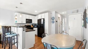Une cuisine moderne avec des meubles blancs, un réfrigérateur noir et un coin repas comprenant une table ronde et des chaises.