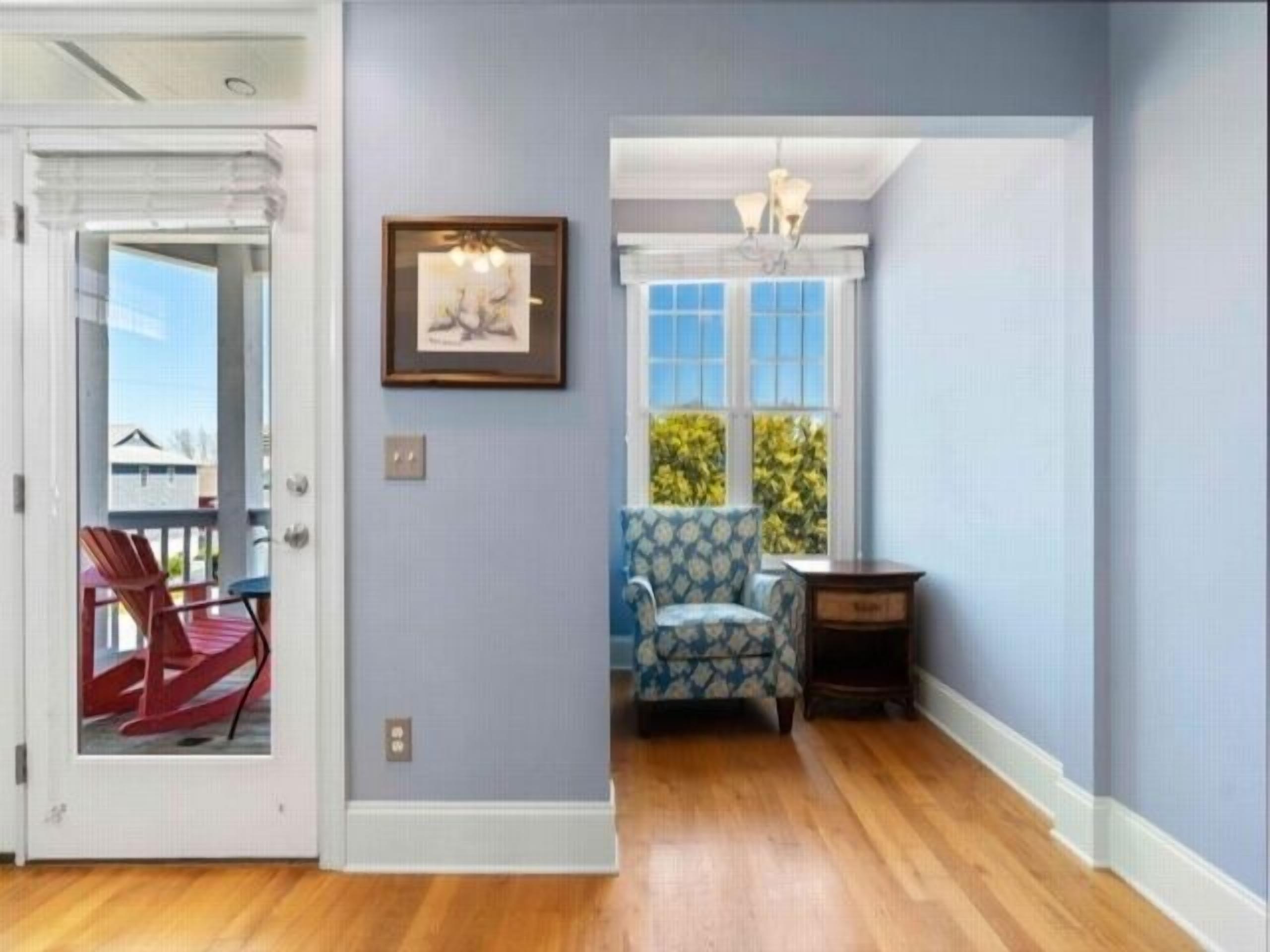 Ein Zimmer mit Holzboden, einem blauen Sessel, einem kleinen Tisch und einem gerahmten Bild an der Wand.