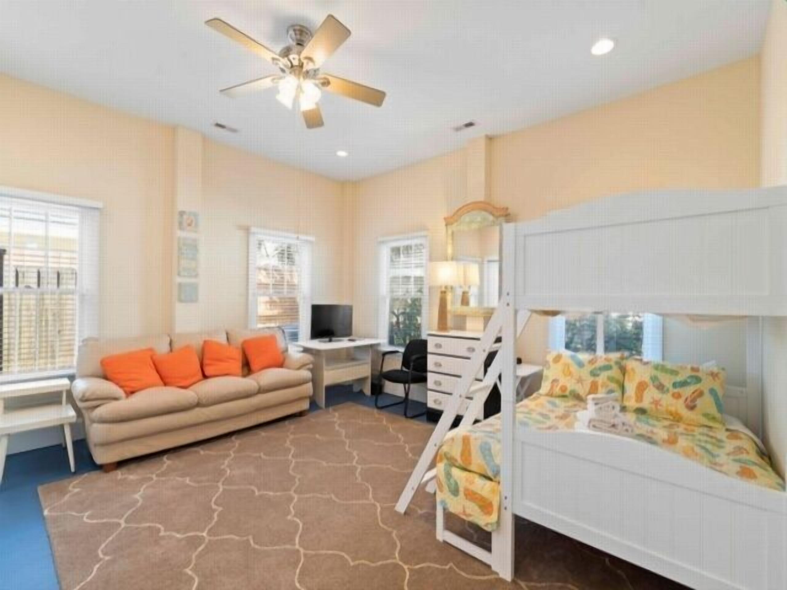 A room with a bunk bed, a sofa, a desk, and a ceiling fan.