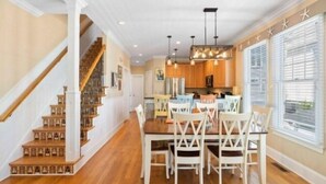 A spacious dining area with a wooden staircase, a kitchen with wooden cabinets, and a large window with blinds. - After Dune Delight - Relax And Unwind In This Fun And Spacious 3 Story Home. Light, Bright, And Close To Everything! 4 Bedroom Townhouse by RedAwning (Carolina Beach)