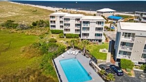 Un hotel moderno con piscina rectangular, varios balcones y vista a la playa y al océano.