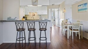 Una cocina moderna con armarios blancos, una isla central con taburetes y un comedor con sillas blancas.