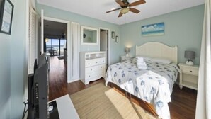 Un dormitorio con cama, ventilador de techo, televisor, cómoda y vistas al exterior.
