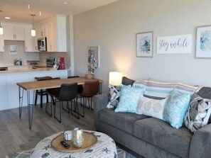 Ein modernes Wohnzimmer mit einem grauen Sofa, einem Holzesstisch und einer Küche im Hintergrund.