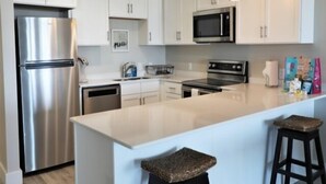 A modern kitchen with white cabinets, stainless steel appliances, and a central island with stools. - Carolina Beach Dreamin - Light Filled South Side End Unit. Ocean Views From Most Rooms! Private Beach Access! 3 Bedroom Condo by Redawning (Carolina Beach)