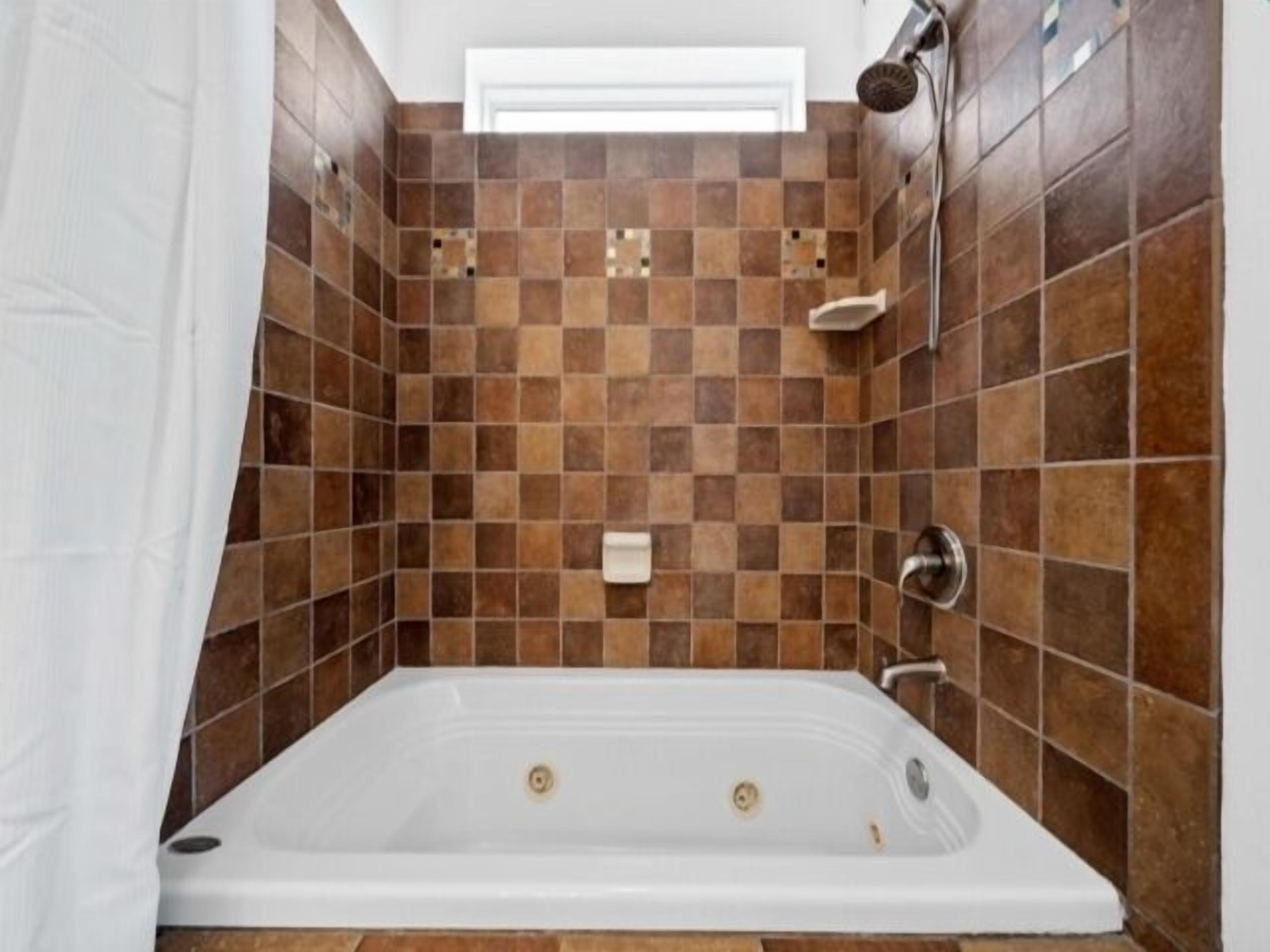 A bathroom with a white bathtub, checkered brown tiles, a showerhead, and a white towel rack.