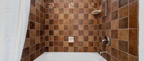 A bathroom with a white bathtub, checkered brown tiles, a showerhead, and a white towel rack.