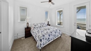 Una camera da letto con un letto, una ventola a soffitto, un comò e due finestre con tende.