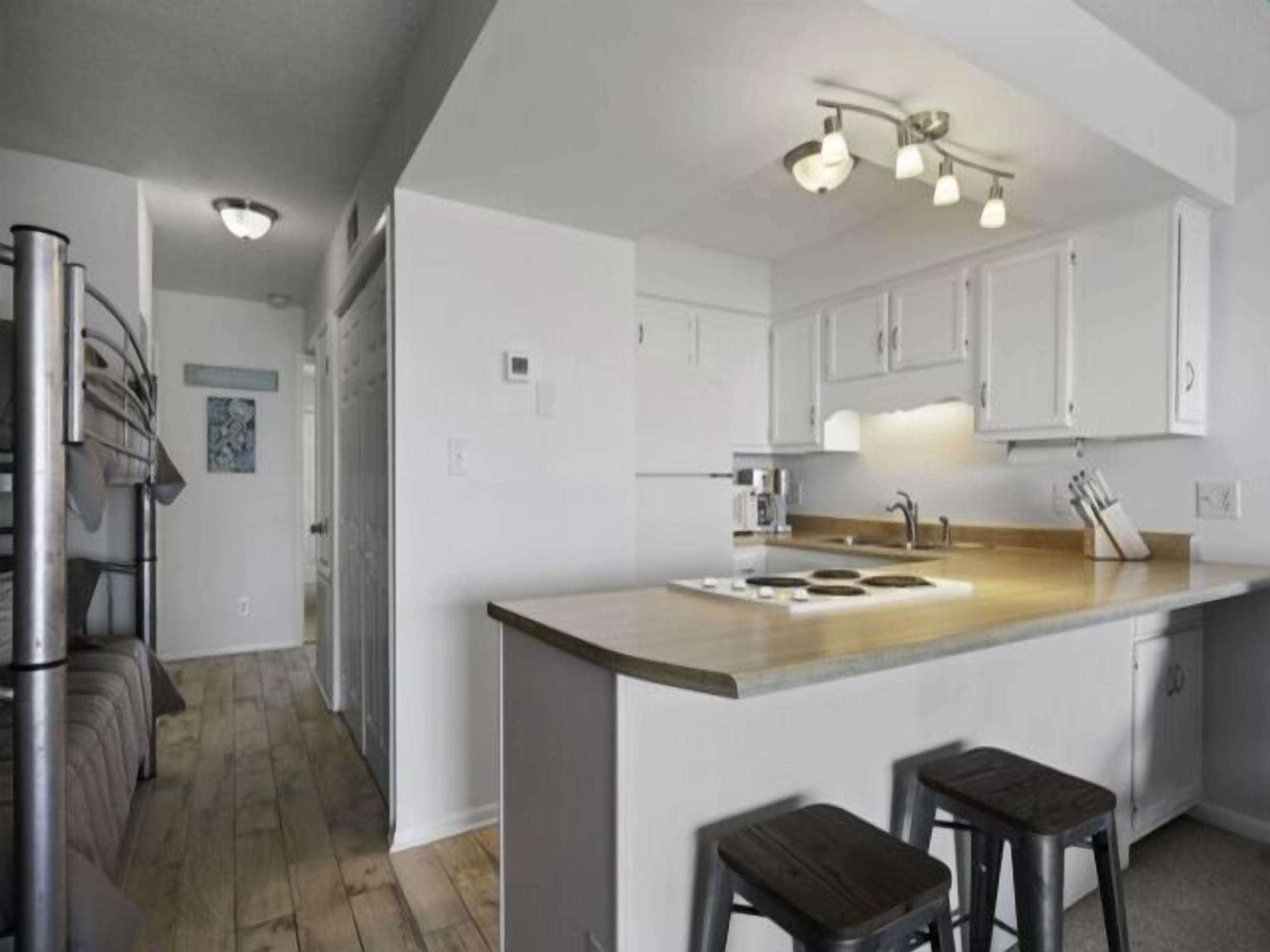 Una cucina moderna con mobili bianchi, un'isola centrale con sgabelli, elettrodomestici in acciaio inossidabile e un lampadario a soffitto.