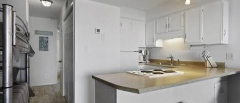 Una cucina moderna con mobili bianchi, un'isola centrale con sgabelli, elettrodomestici in acciaio inossidabile e un lampadario a soffitto.