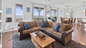 A spacious living room with a large sectional sofa, a wooden coffee table, and a ceiling fan. - A Shore Thing 2 - Oceanfront And Pet Friendly Home - See The Sunrise, Hear The Waves, Feel The Breeze - Large Oceanfront Balcony 6 Bedroom Townhouse by RedAwning (Carolina Beach)