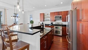 A modern kitchen with wooden cabinets, stainless steel appliances, and a central island with seating. - A Shore Thing 2 - Oceanfront And Pet Friendly Home - See The Sunrise, Hear The Waves, Feel The Breeze - Large Oceanfront Balcony 6 Bedroom Townhouse by RedAwning (Carolina Beach)