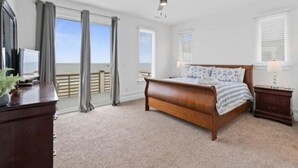 A bedroom with a large bed, a ceiling fan, and a view of the ocean through the sliding glass doors. - A Shore Thing 2 - Oceanfront And Pet Friendly Home - See The Sunrise, Hear The Waves, Feel The Breeze - Large Oceanfront Balcony 6 Bedroom Townhouse by RedAwning (Carolina Beach)