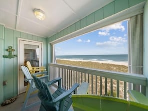 Une véranda avec vue sur la plage, comprenant une porte, un banc et plusieurs chaises.