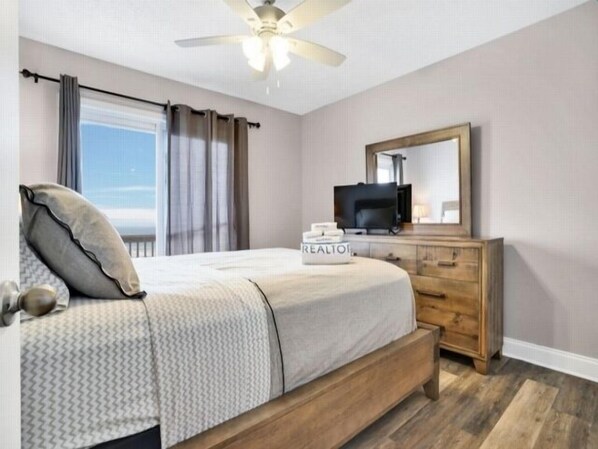 A bedroom with a bed, a television, a dresser, and a ceiling fan.