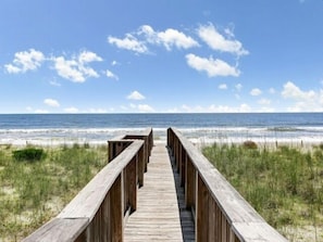 A wooden boardwalk leading to a beach with a clear sky and ocean in the background.