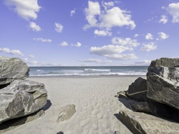A beach with large rocks in the foreground and the ocean in the background.