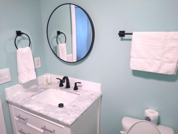 A bathroom with a white sink, black faucet, a round mirror, and a towel rack.