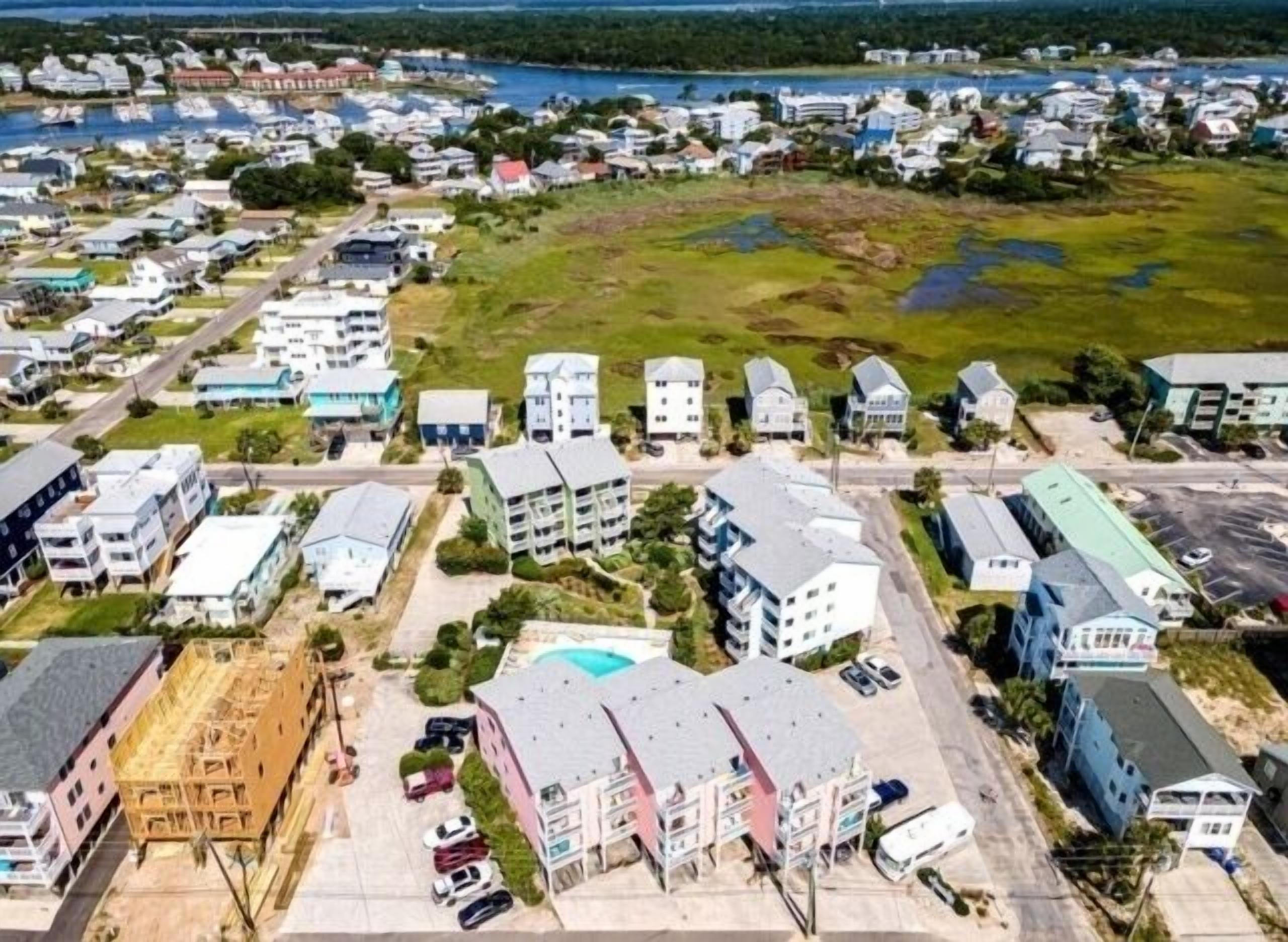 Vista aérea de una zona residencial con varios edificios de apartamentos, un estacionamiento y una masa de agua al fondo.