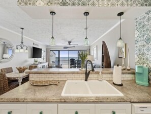 Een moderne keuken met een groot eiland, hanglampen en uitzicht naar buiten.