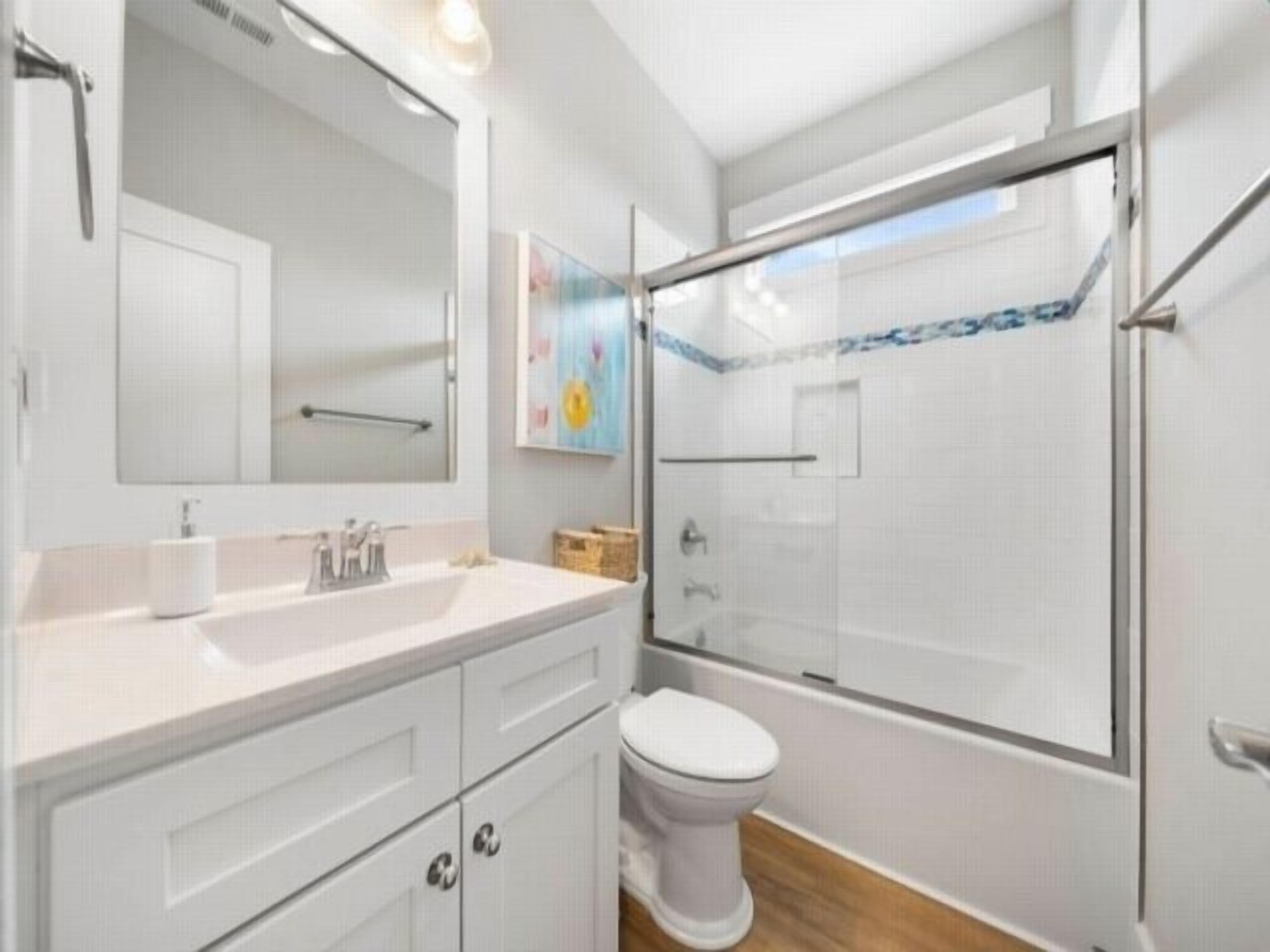 Une salle de bain moderne avec une douche à parois de verre, des toilettes blanches et un meuble-lavabo avec un miroir.