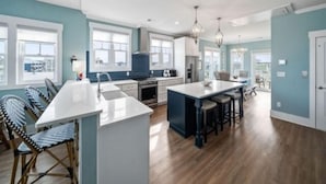 A spacious kitchen with a large island, wooden flooring, and a view of the outdoors through large windows.