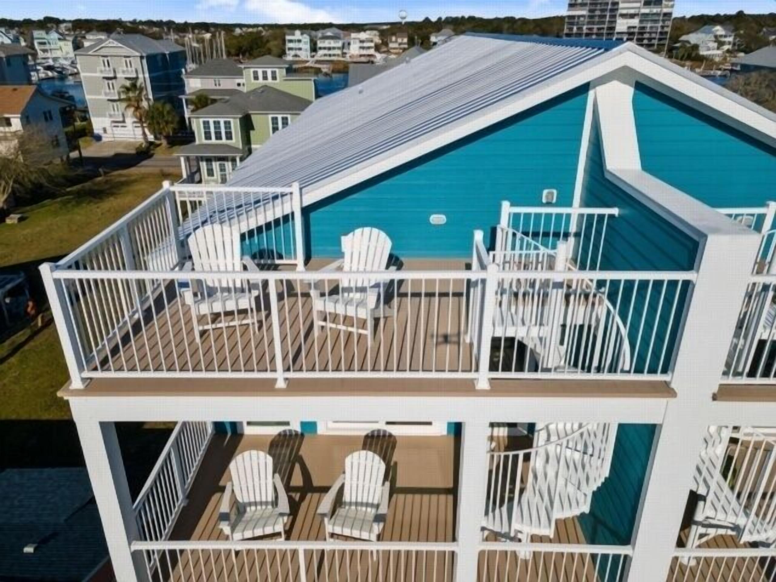 A two-story building with a swimming pool on the upper level, surrounded by white railings and furnished with Adirondack chairs.