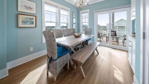 A dining room with a wooden table and chairs, large windows, and a chandelier.