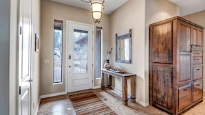 A hallway with a wooden cabinet, a console table with a vase and a plate, and a door with a stained glass design.